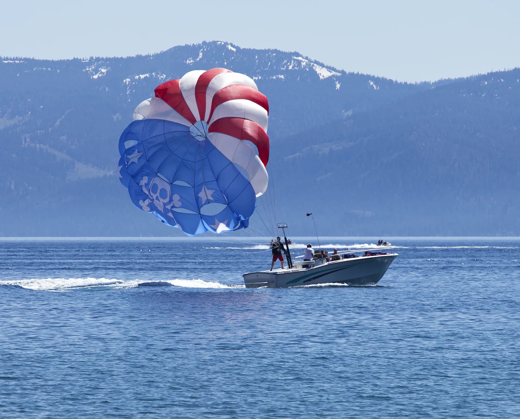 A red, white and blue parasail towed by a boat across a mountain lake